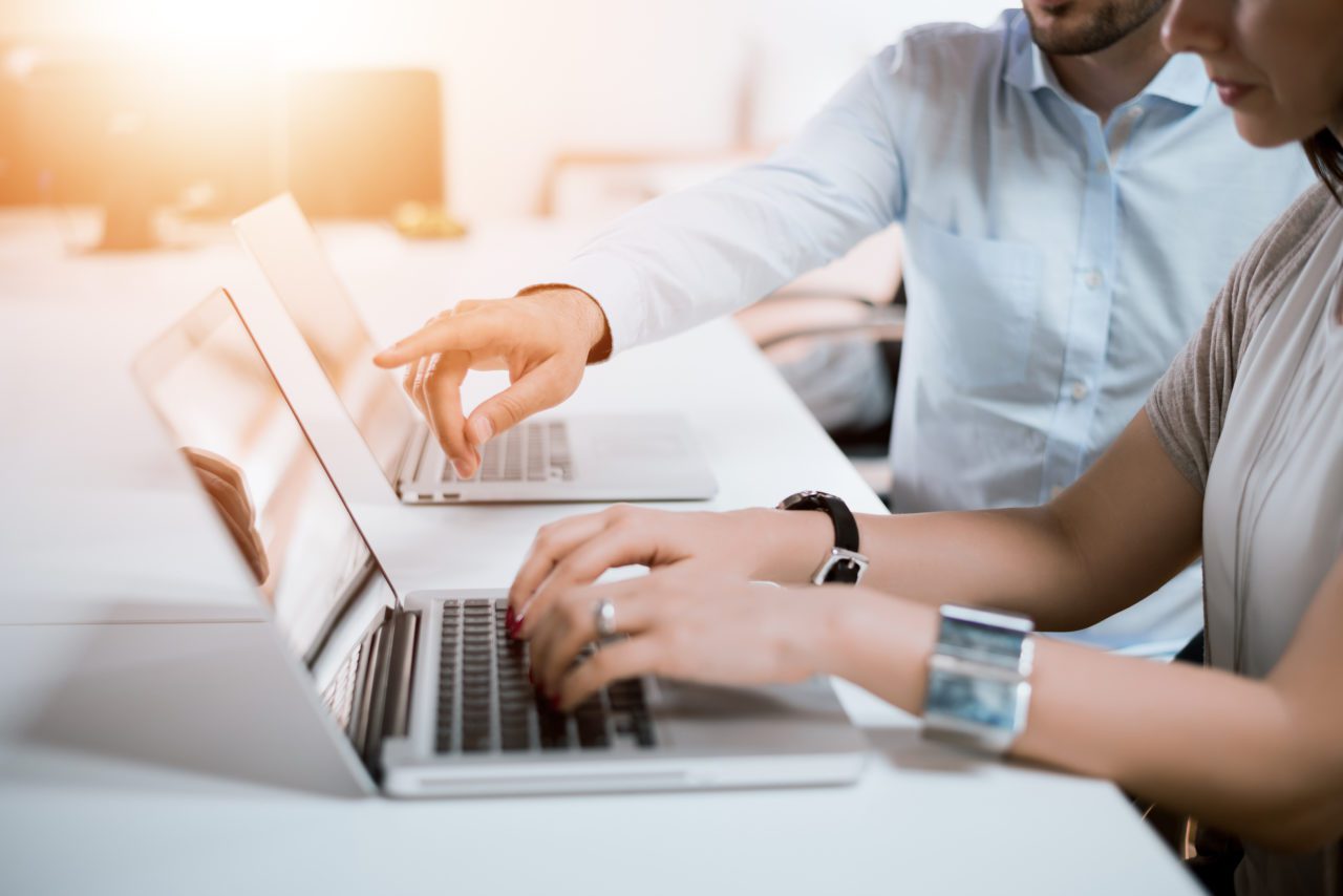 Woman and man sit at a table together sharing business ideas through laptops set in front of them