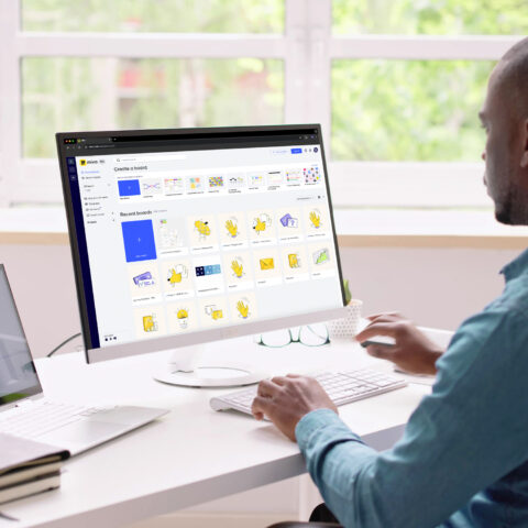 A photo of a professional man sitting at a work desk using the Miro software on his computer.