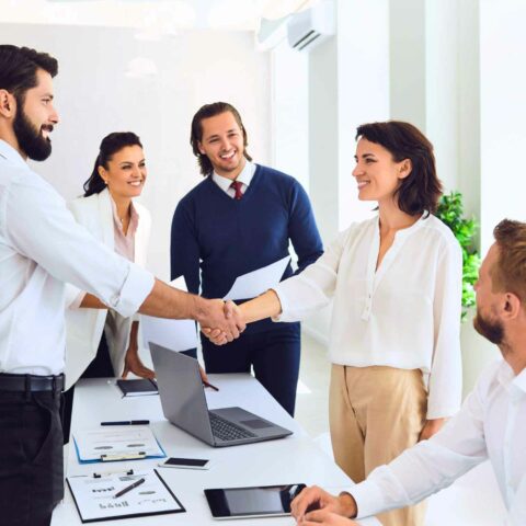 A group of UX Professionals standing around a table in a business environment, shaking hands.