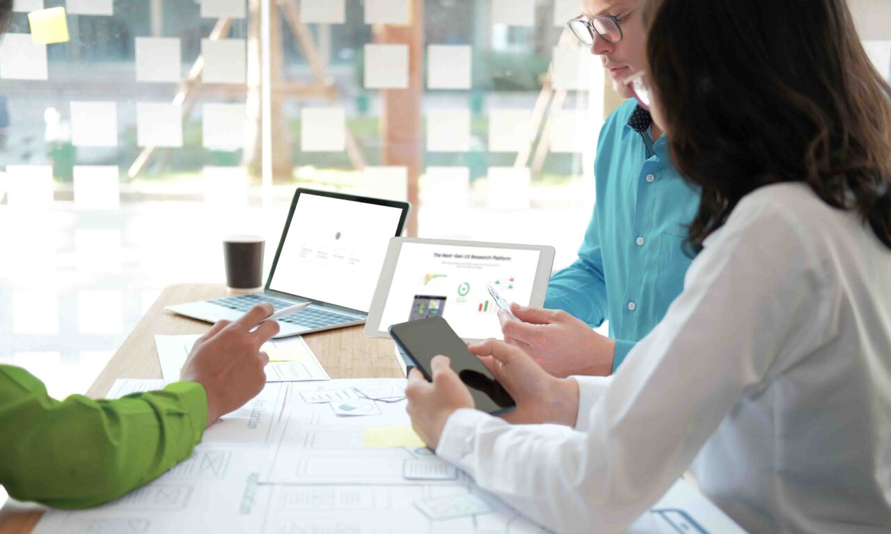 An image of three UX designers sitting around a table working collaboratively using graphs, diagrams, and AI technology.