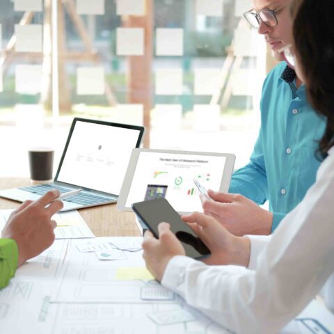 An image of three UX designers sitting around a table working collaboratively using graphs, diagrams, and AI technology.