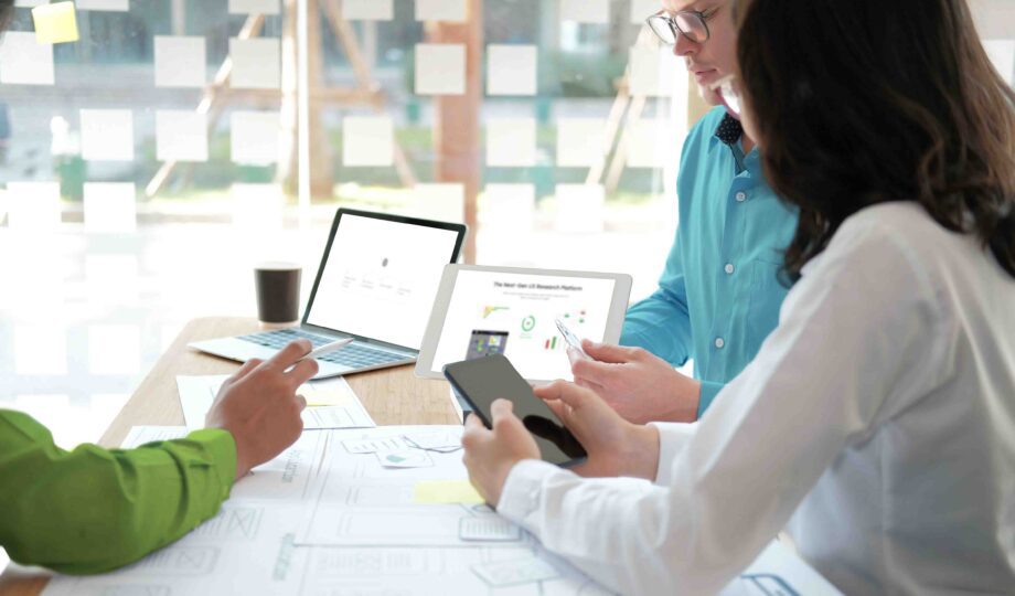 An image of three UX designers sitting around a table working collaboratively using graphs, diagrams, and AI technology.