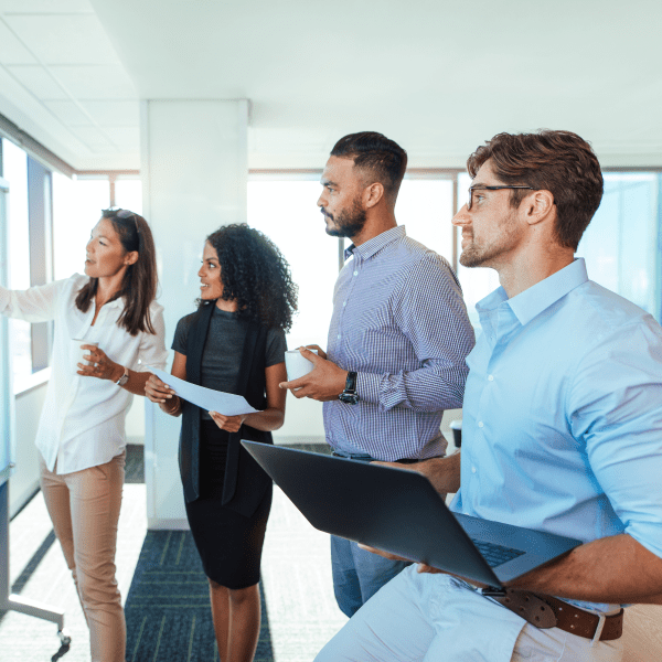 Four coworkers standing together while one team member presents at a whiteboard.